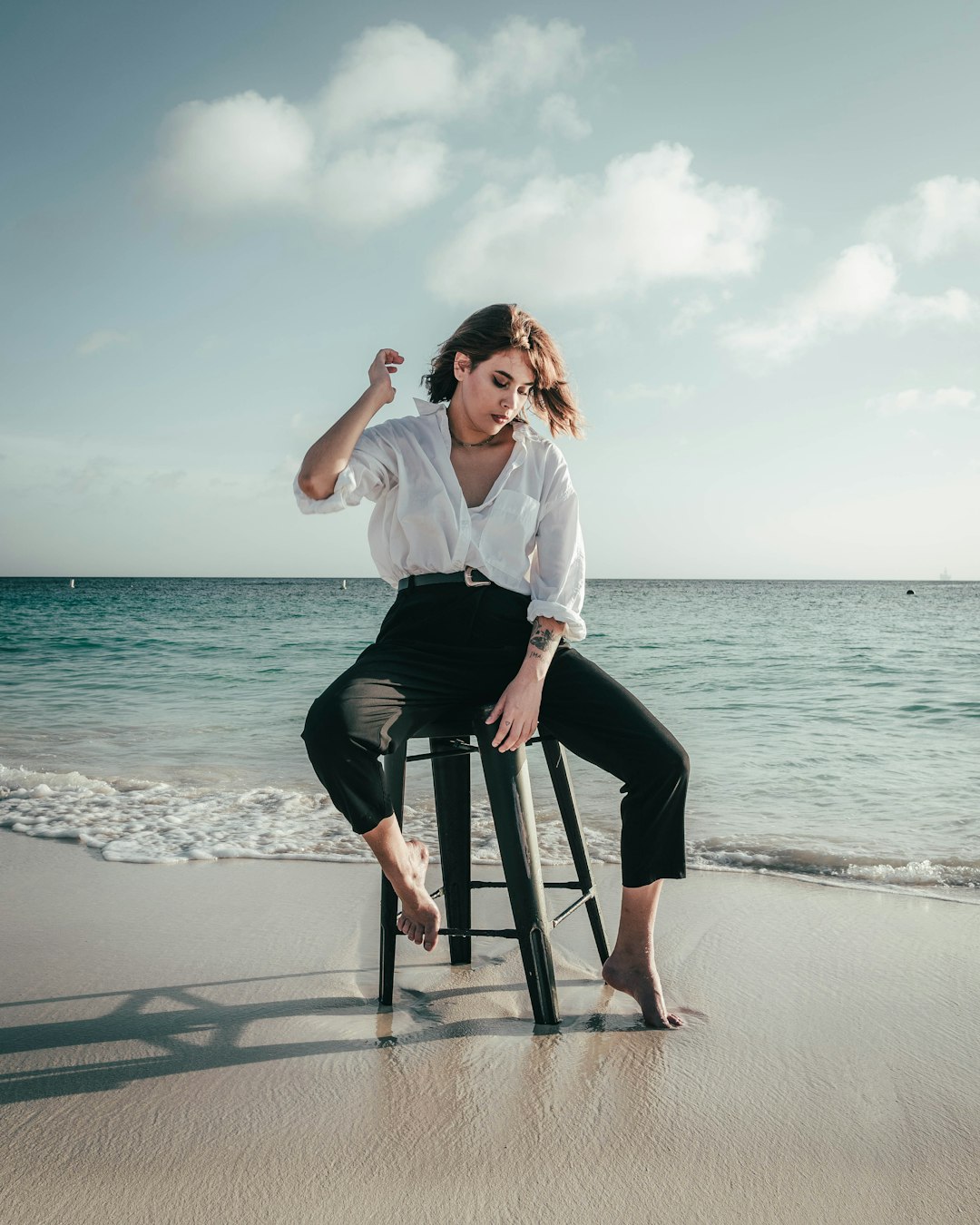 woman in white shirt and black pants sitting on black wooden chair on beach during daytime