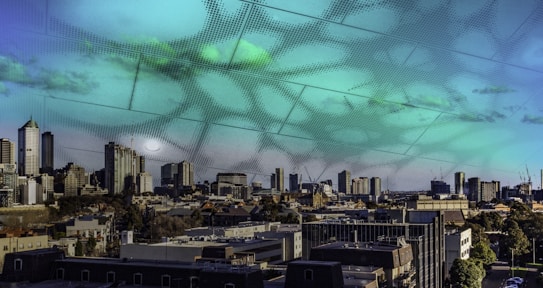A city skyline with numerous high-rise buildings and skyscrapers. The sky features a surreal overlay with patterns and hues of green and blue, giving it an artistic and futuristic appearance.