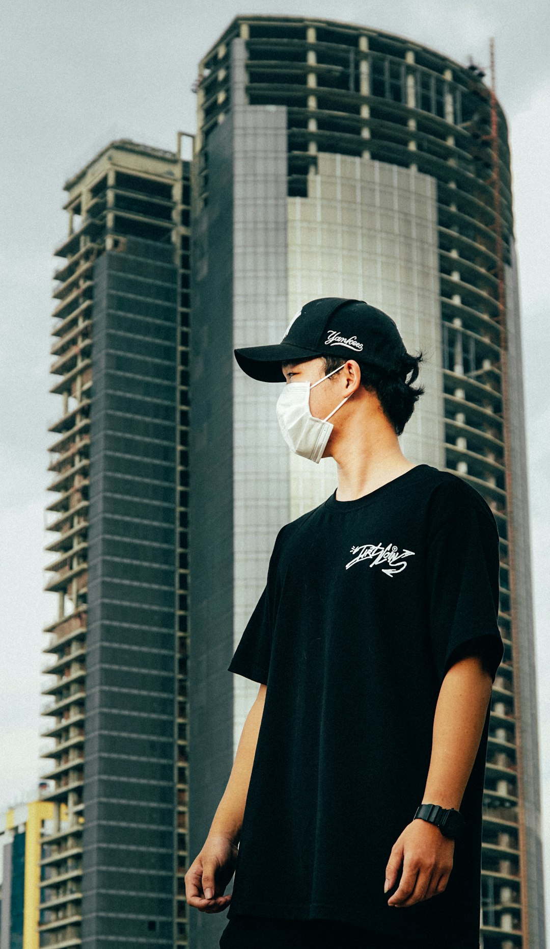man in black crew neck t-shirt wearing black cap standing near building during daytime