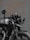 A black motorcycle is parked in front of a corrugated metal door. The bike features a round headlight, a rearview mirror with a logo, and a visible license plate. Details of the suspension and exhaust system are noticeable, and the paint on the vehicle appears to be well-maintained.