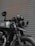 A black motorcycle is parked in front of a corrugated metal door. The bike features a round headlight, a rearview mirror with a logo, and a visible license plate. Details of the suspension and exhaust system are noticeable, and the paint on the vehicle appears to be well-maintained.