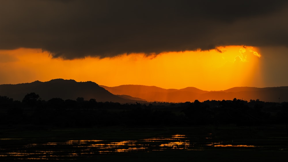 silhouette of mountain near body of water during sunset