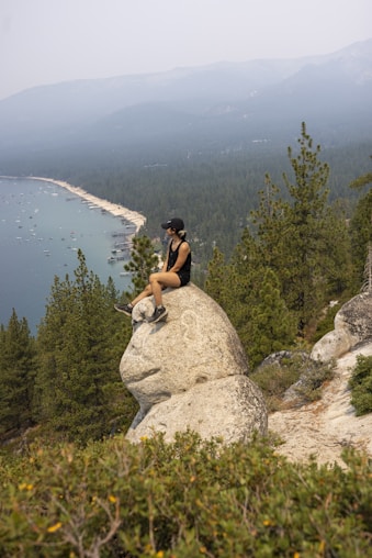man in black t-shirt sitting on rock near lake during daytime