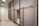 A room with multiple bunk beds, each enclosed with gray curtains for privacy. The beds are structured with black metal frames, and ladders are attached to access the upper bunks. The walls are white, and there's a full-length mirror on one wall. Ceiling lights with black shades provide illumination.