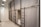 A room with multiple bunk beds, each enclosed with gray curtains for privacy. The beds are structured with black metal frames, and ladders are attached to access the upper bunks. The walls are white, and there's a full-length mirror on one wall. Ceiling lights with black shades provide illumination.