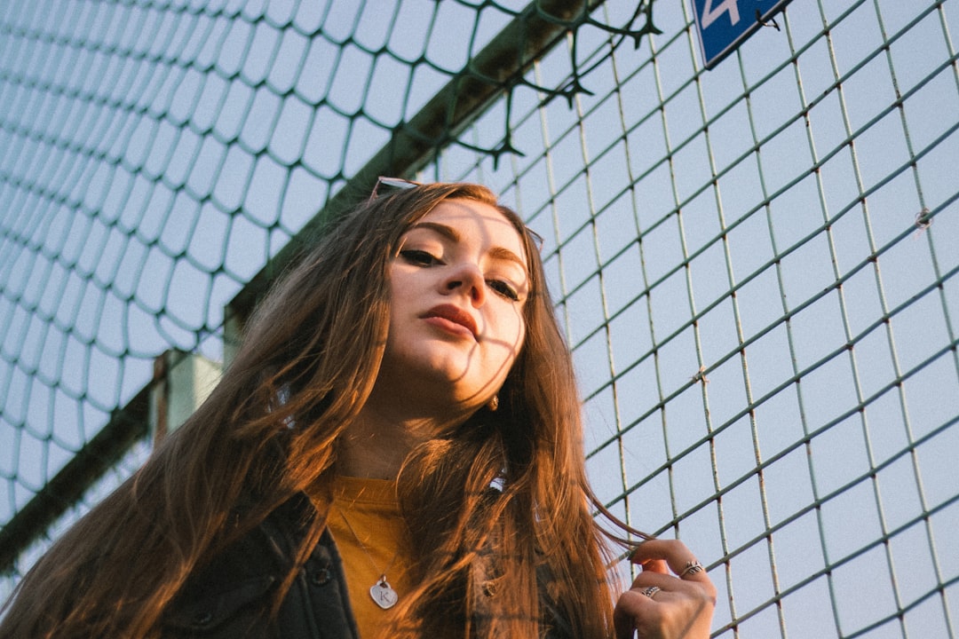 woman in black jacket standing beside chain link fence