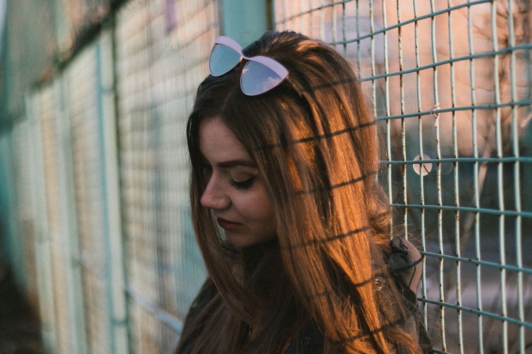 woman in black sunglasses standing near brown metal fence during daytime