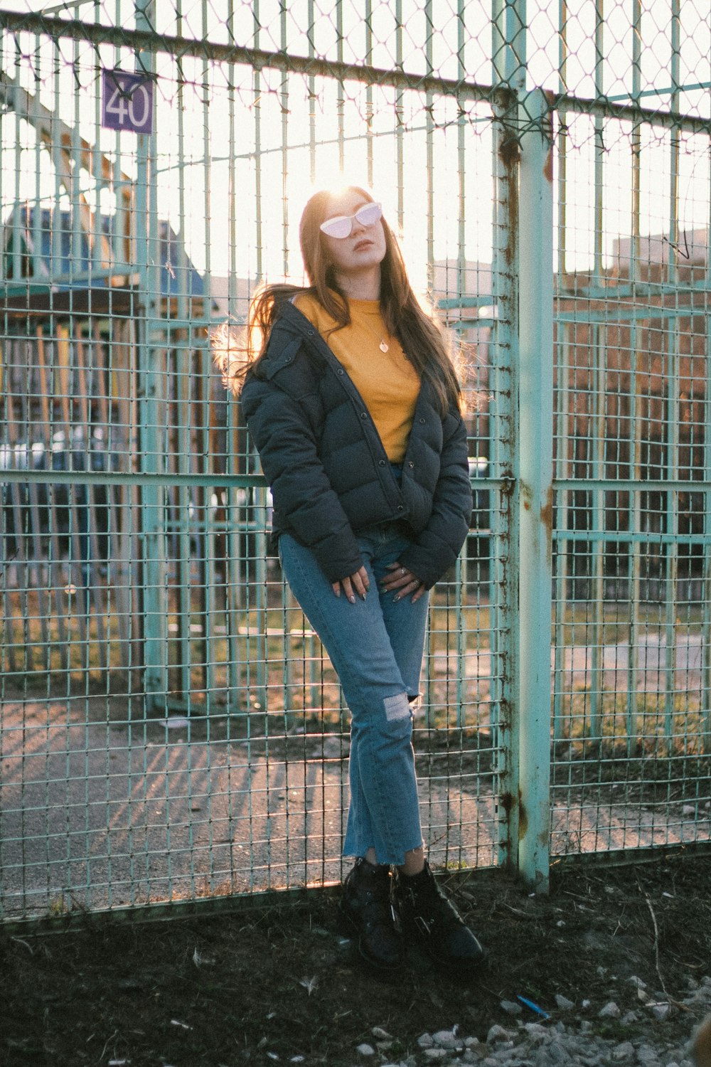 woman in black jacket and blue denim jeans standing near blue metal fence during daytime