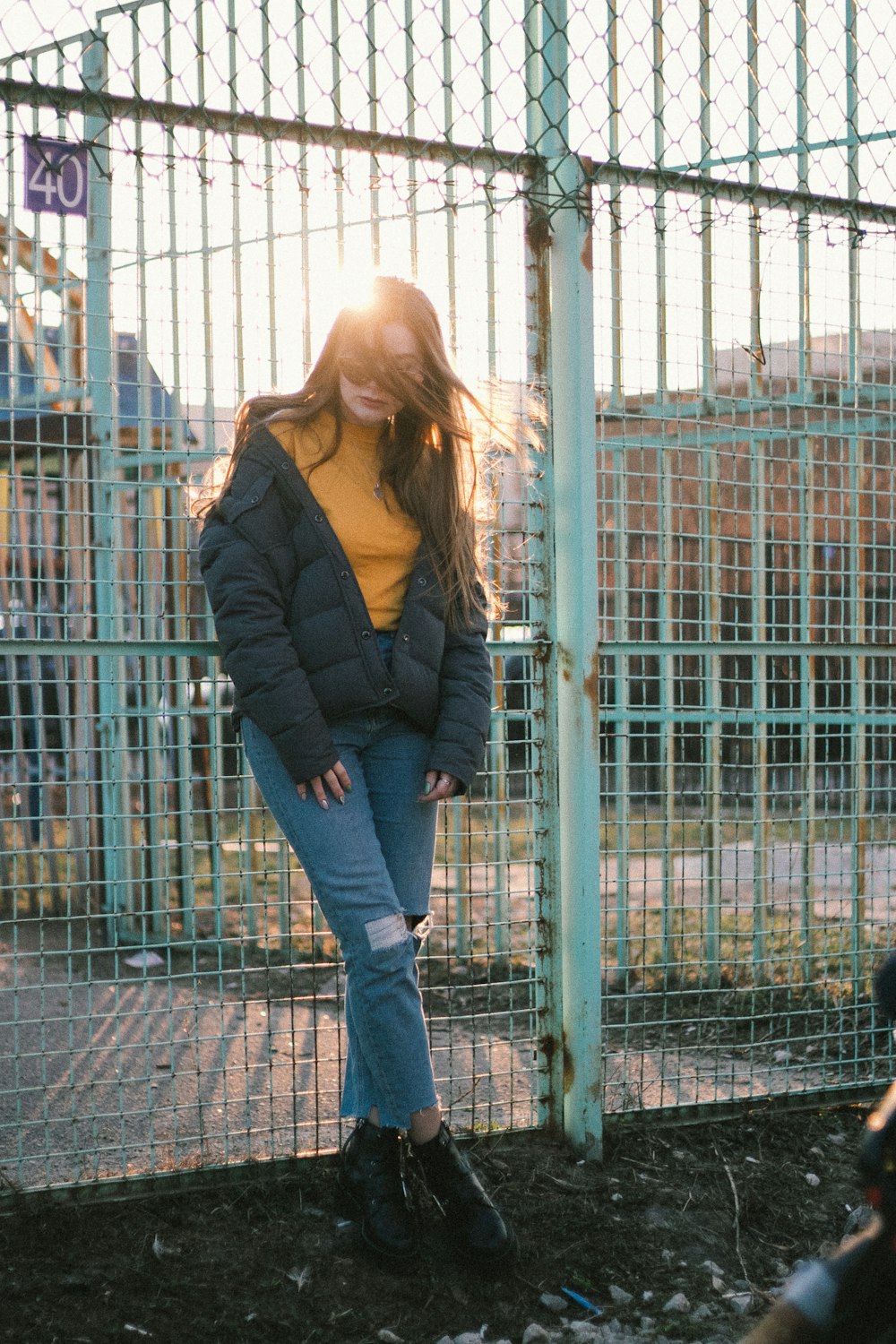 woman in black jacket and blue denim jeans standing near blue metal fence during daytime