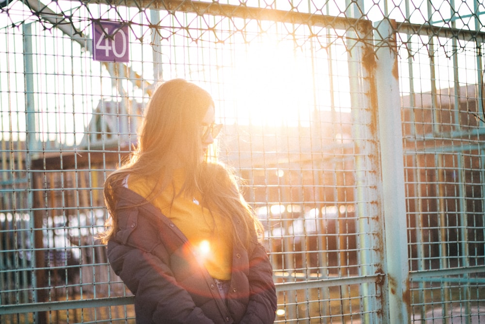 woman in black jacket standing beside white metal fence during daytime