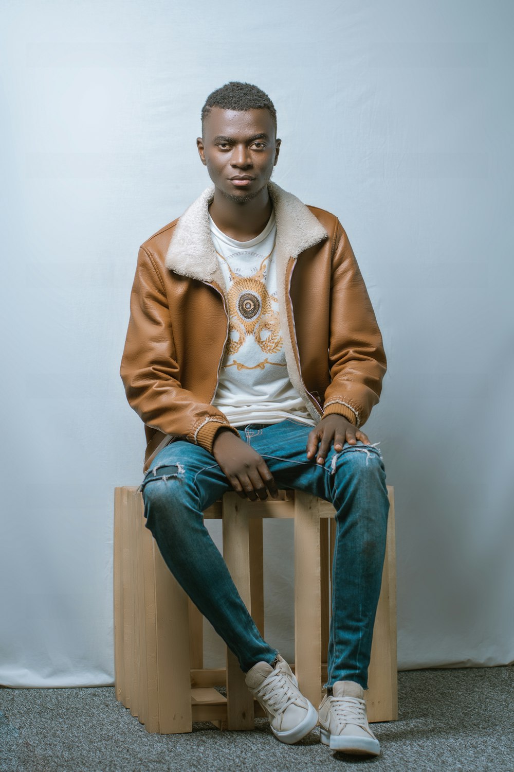 man in brown blazer and blue denim jeans sitting on brown wooden seat