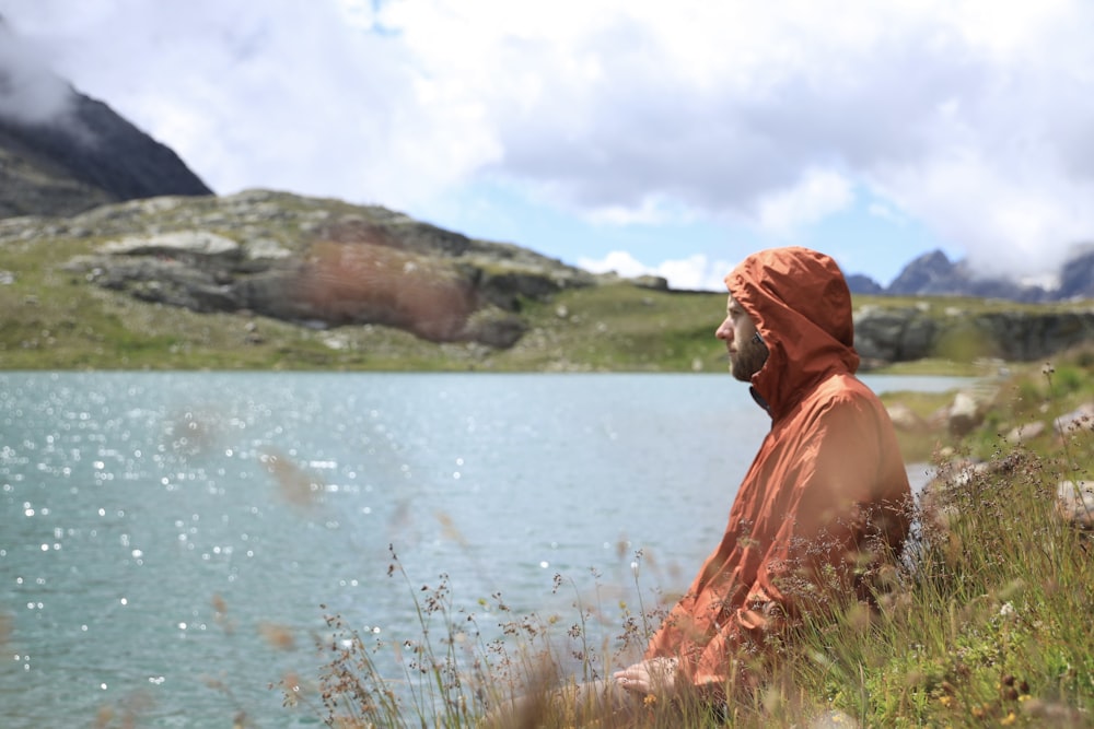 woman in orange hijab standing on green grass near body of water during daytime