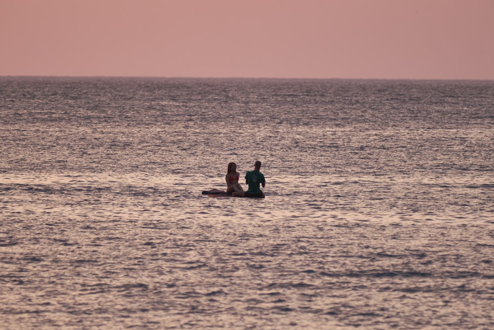 2 person sitting on the beach during sunset