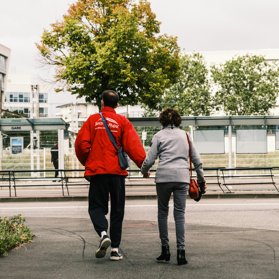 man in orange jacket and gray pants walking with woman in gray jacket