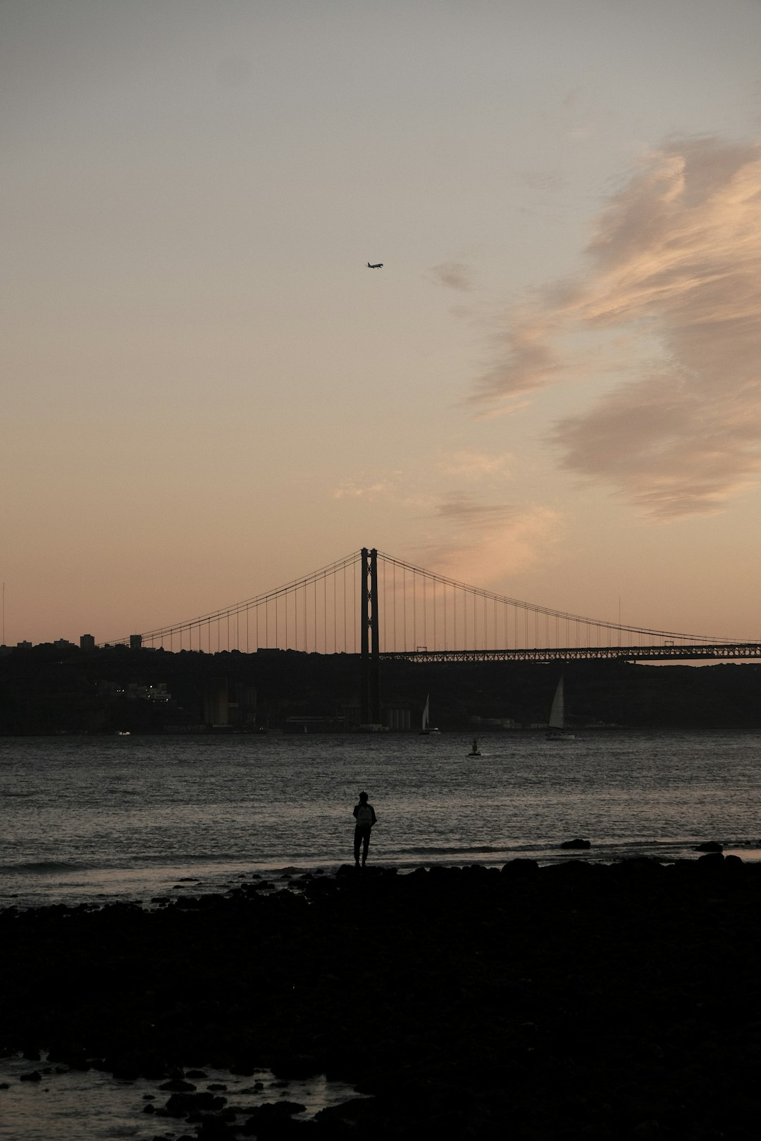 silhouette of person standing on seashore near bridge during sunset