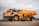 A large, heavy-duty yellow dump truck is positioned on a paved surface, carrying a load of material in its bed. The truck is branded with Volvo and appears to be used in construction or mining. The background features a cloudy sky and some sparse vegetation.