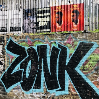 A brick wall features vibrant graffiti with the word 'ZONK' painted in bold black letters outlined in blue. Above the graffiti, several music posters are displayed on a metal fence, promoting albums by Yung Bleu and another artist.