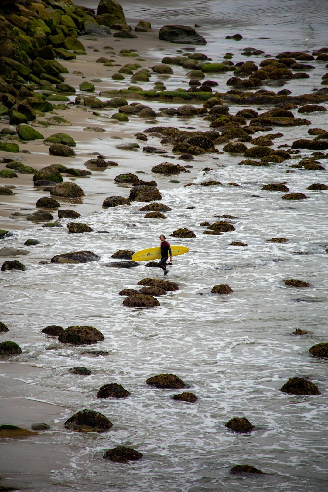 person in yellow shirt and black pants standing on rocky shore during daytime