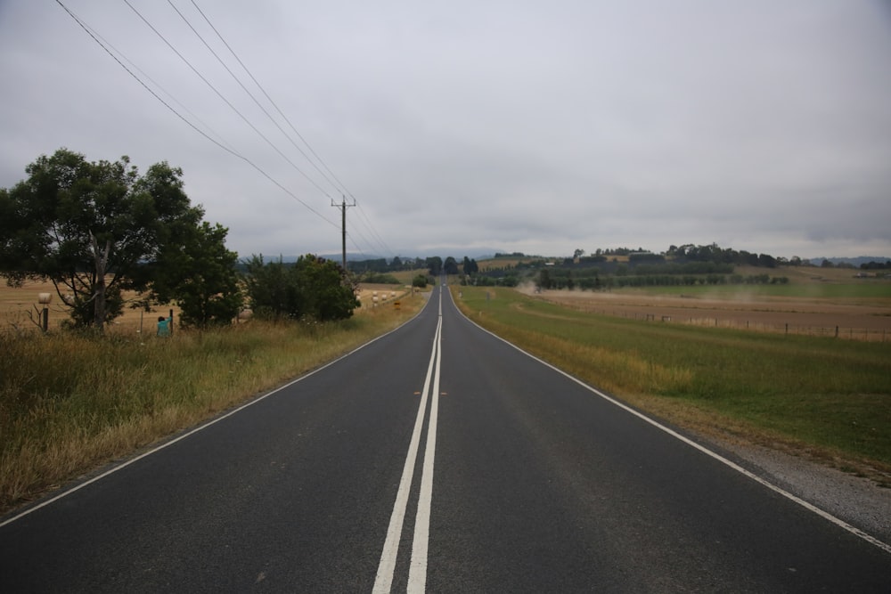 gray concrete road between green grass field under white clouds during daytime