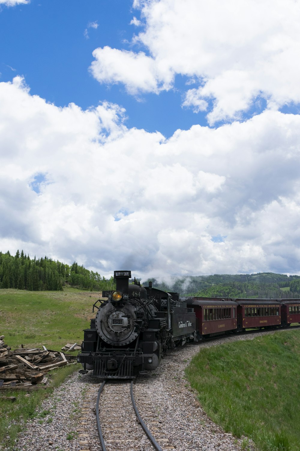 昼間、白い雲と青い空の下、線路を走る黒と赤の列車