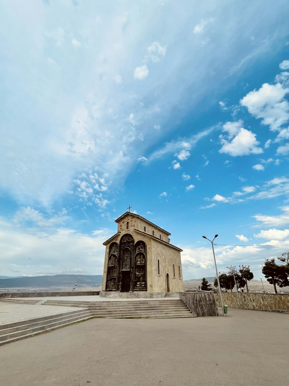 people walking on sidewalk near brown concrete building under blue and white sunny cloudy sky during