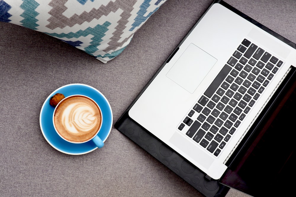 white ceramic mug with coffee beside macbook pro