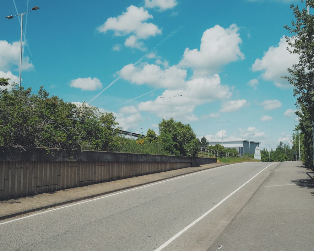 green trees beside gray concrete road under blue sky and white clouds during daytime