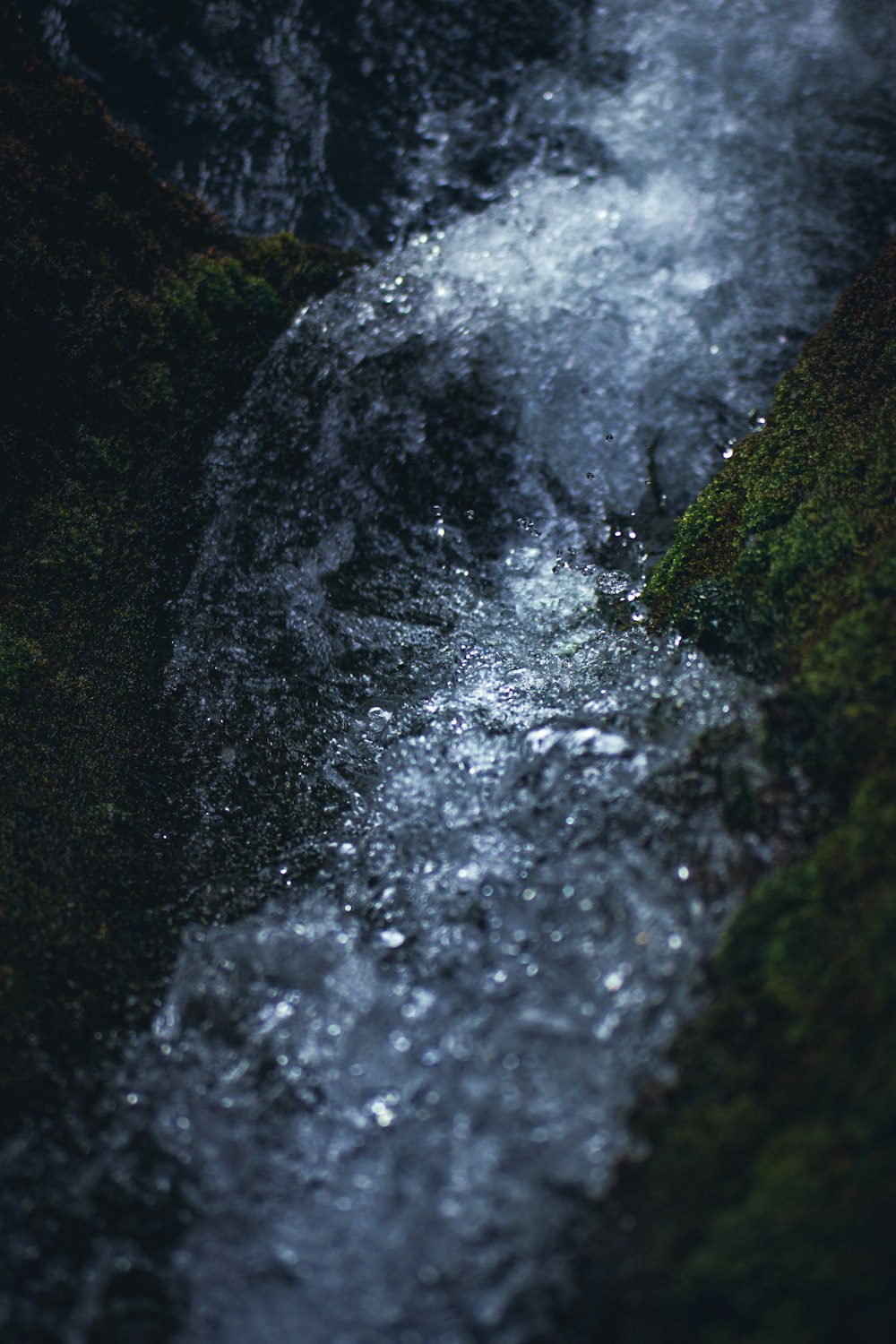 water falls in the middle of green moss covered rocks