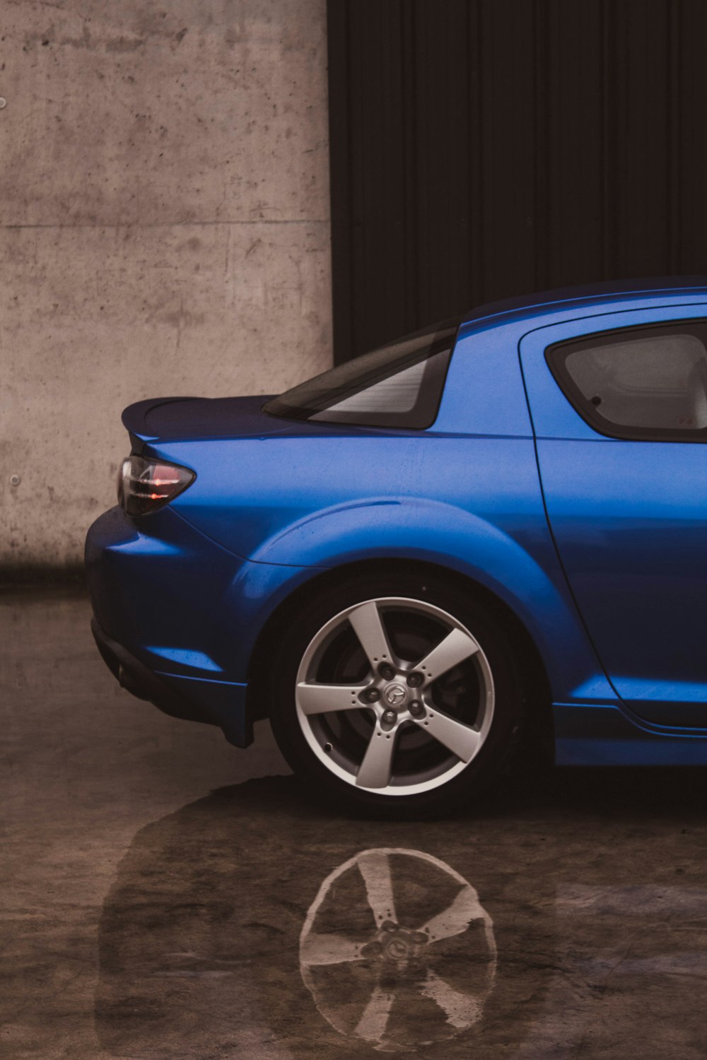 blue car parked beside gray wall