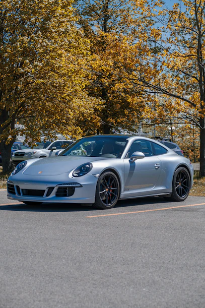 silver porsche 911 parked on gray concrete road near green trees during daytime