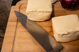 Elegant block of tofu on a wooden board with subtle peacock feather pattern beneath.