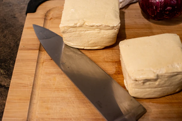 Elegant block of tofu on a wooden board with subtle peacock feather pattern beneath.