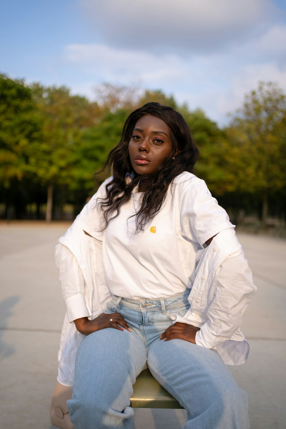 woman in white dress shirt and blue denim jeans sitting on road during daytime