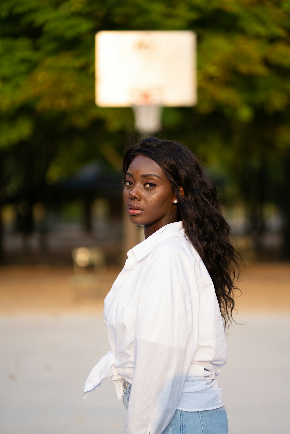 woman in white dress shirt standing near green trees during daytime