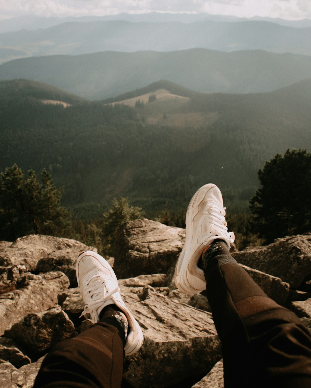 person in black pants and white sneakers sitting on rock during daytime