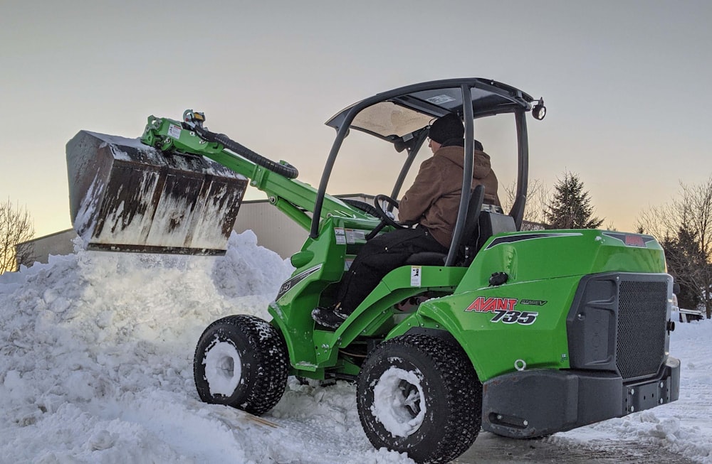 日中、雪に覆われた地面で芝刈り機に乗る緑と黒のJohn Deere社