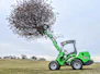 A compost turner working through piles of green waste under a clear sky.