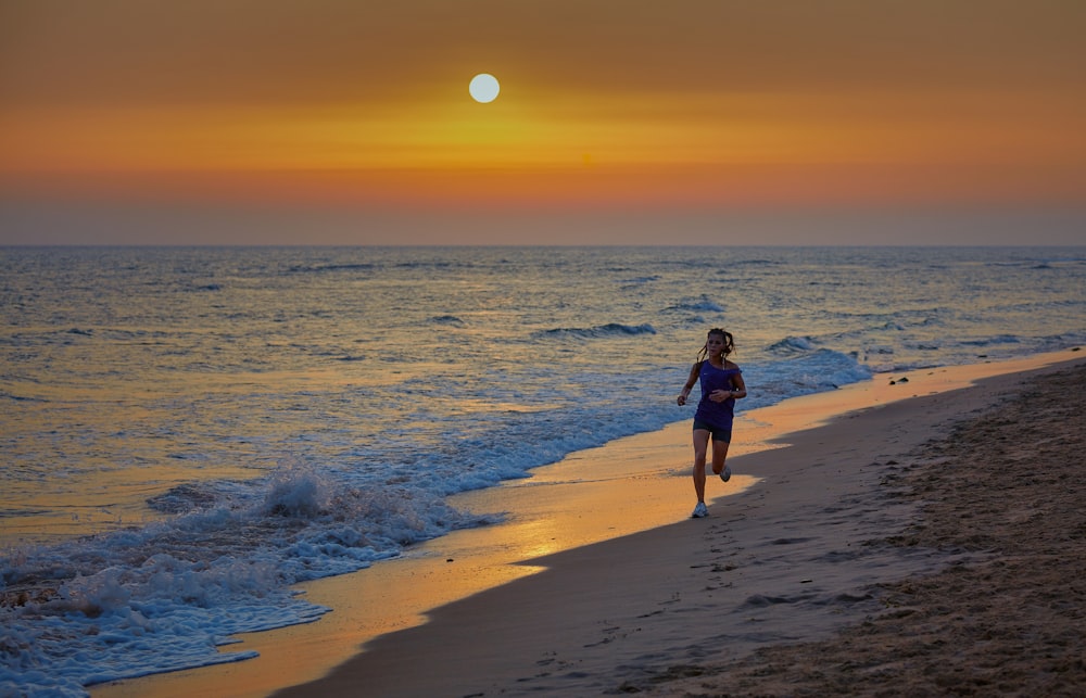 Mujer en vestido negro caminando en la playa durante la puesta del sol