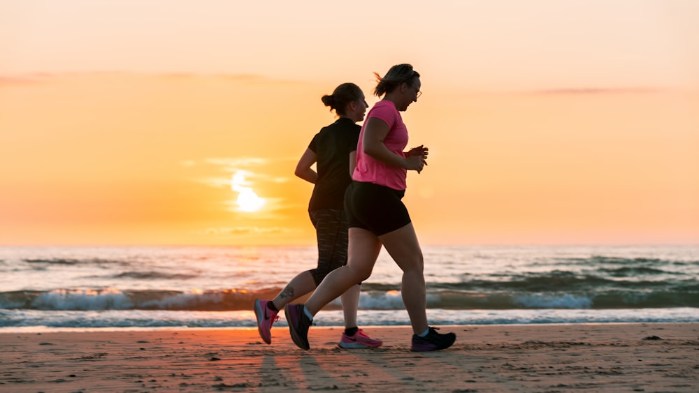 Mujer en camiseta sin mangas negra y pantalones cortos negros corriendo en la playa durante la puesta del sol