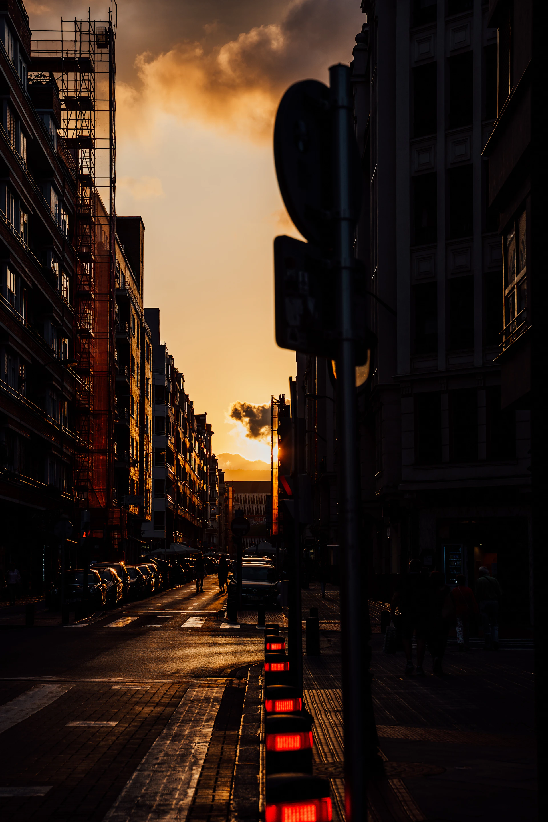 An urban street scene at sunset, framed centrally to keep all buildings and lights in natural proportion.