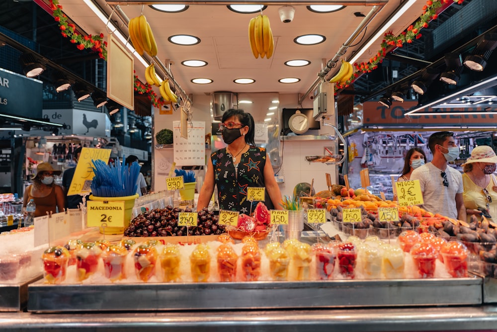 Femme en robe fleurie noire et blanche debout devant le stand de fruits