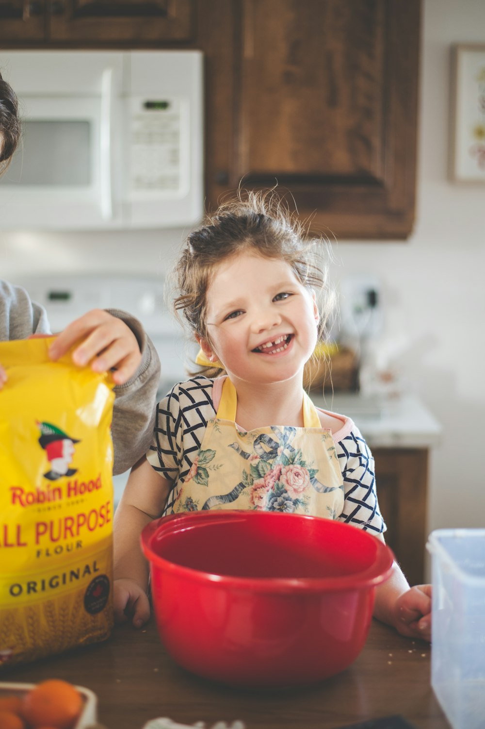 girl in white and black floral shirt holding yellow plastic container