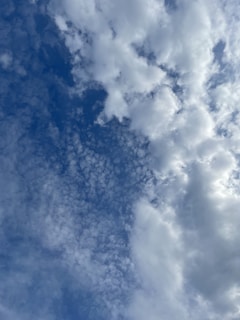 A cloudy sky featuring a variety of cloud formations, including fluffy cumulus clouds and smaller, scattered cirrus clouds all set against a backdrop of blue sky. The clouds range in density, creating a dynamic and textured appearance.