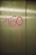 Pink graffiti numbers are painted on a metallic, possibly elevator, door with noticeable paint drips underneath the numbers.