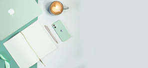 An overhead shot of a cream white desk with a mocha beige cwtch bag, a coffee cup, and scattered notes.