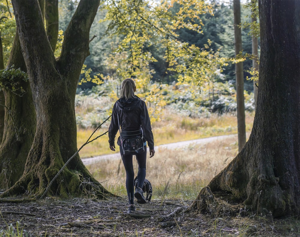 woman in black jacket and black pants walking on forest during daytime