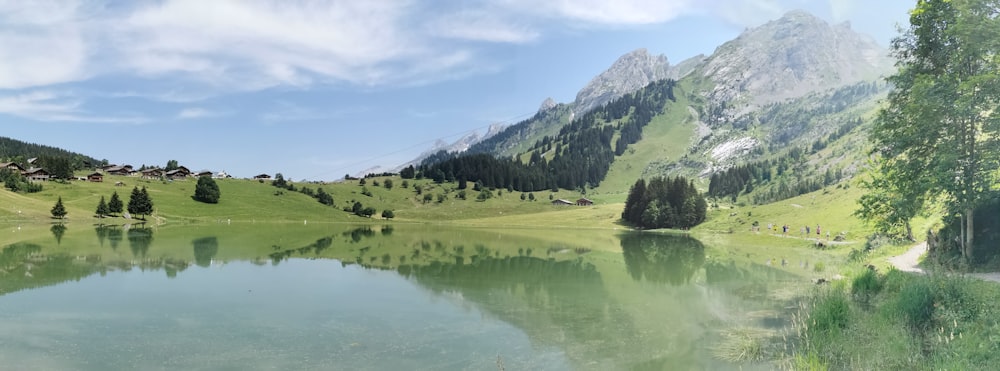 Grünes Grasfeld in der Nähe von See und Berg unter blauem Himmel tagsüber