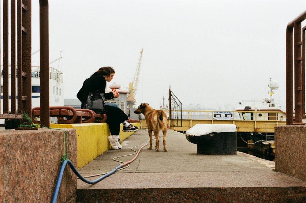 woman in black jacket sitting beside brown dog during daytime