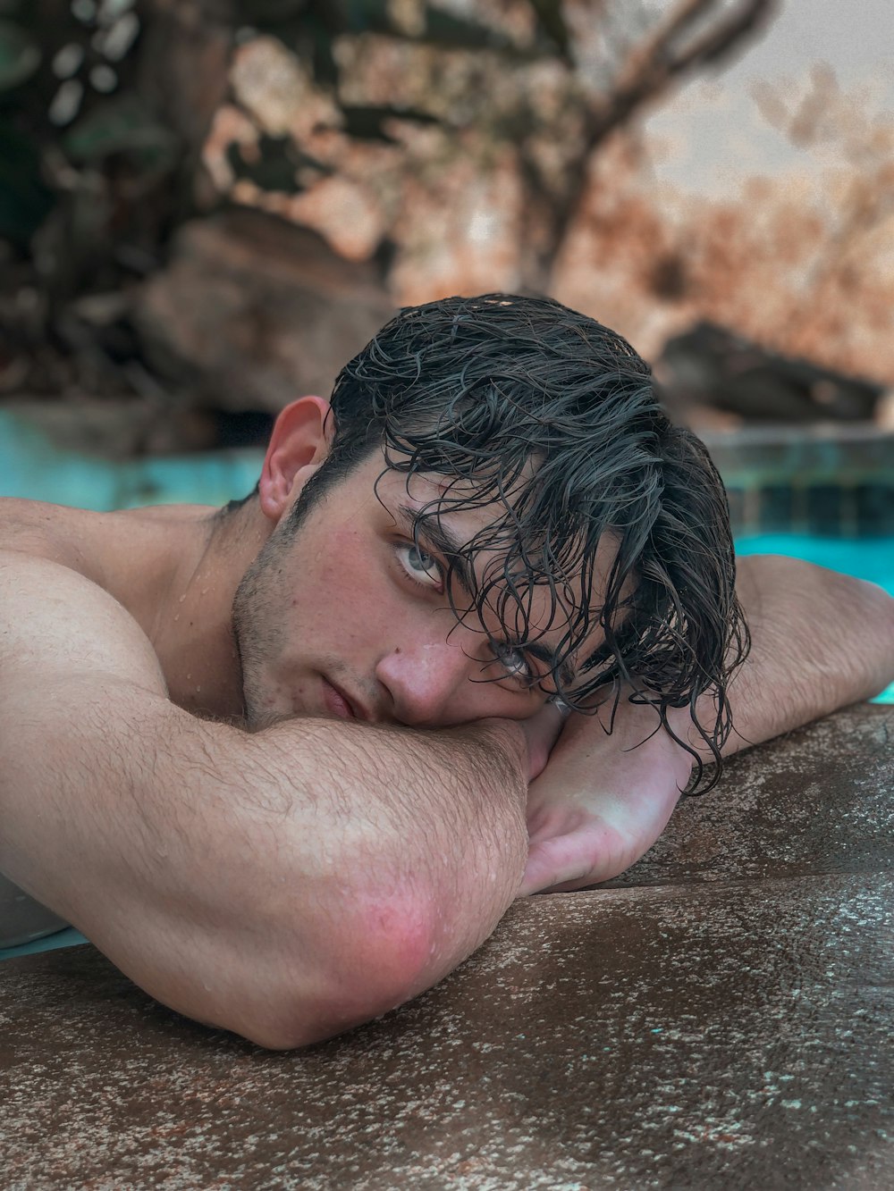 topless man lying on brown sand near swimming pool during daytime