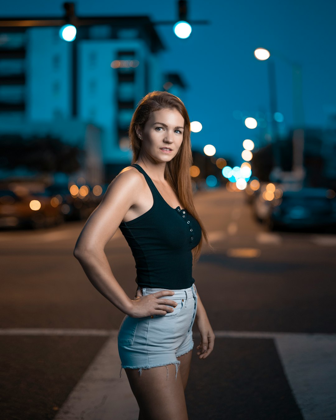 woman in black tank top and blue denim daisy dukes standing on road during night time